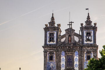 Fototapeta premium Plano detalle de las torres campanario de la barroca Iglesia de San Ildefonso, decorada con tradicionales azulejos azules y blancos bajo una suave luz de atardecer en Oporto, Portugal.