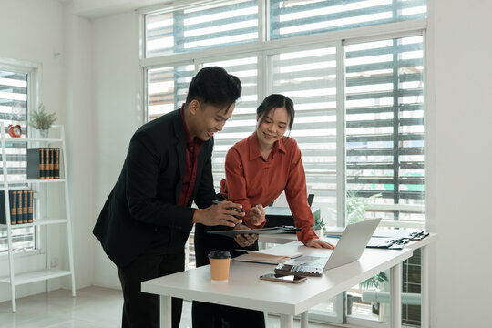 Business Colleagues Standing at Desk Reviewing Clipboard Document and Laptop