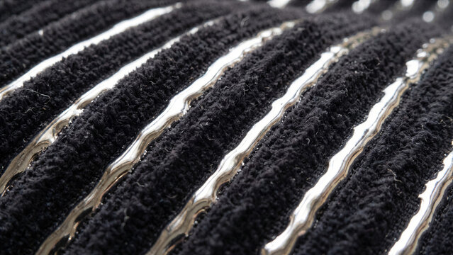Thick textured corduroy fabric surface where parallel ridges alternate between dark matte textile and silver хrome
