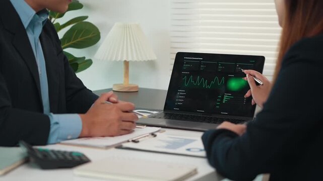 Financial advisors analyzing stock market data on a laptop and discussing investment strategies during a business meeting