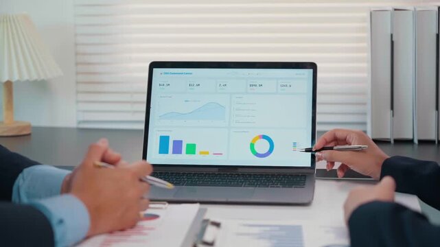 Business professionals analyzing data and discussing financial charts on a laptop screen during a corporate meeting