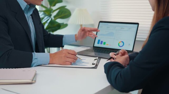 Business colleagues reviewing financial data with charts on a laptop and documents during a strategy meeting in the office