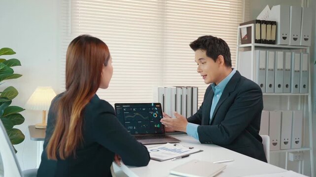 Asian businessman discussing financial data on a laptop with a female colleague during an office meeting