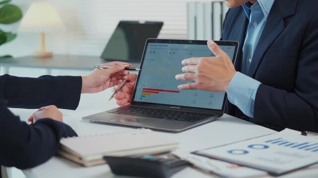 Financial analyst presenting business data chart on laptop screen during corporate meeting with colleague in modern office
