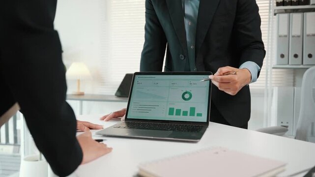 Business colleagues analyzing financial data on a laptop screen with charts and graphs in a modern office meeting