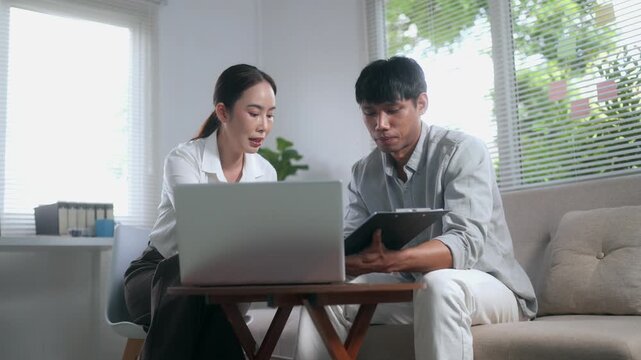 Asian business colleagues collaborating on a project using a laptop and clipboard in a modern office