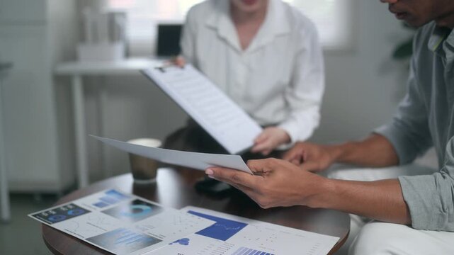 Discussing strategy while reviewing financial charts and graphs, two business colleagues sit at a table in a modern office