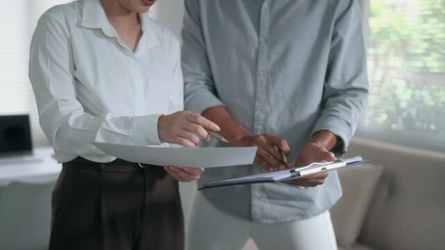 Two business colleagues standing and discussing a project, reviewing documents and talking strategy. Corporate teamwork and planning concept