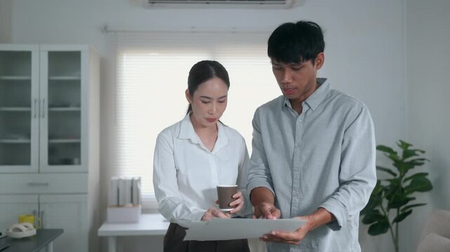 Asian business colleagues discussing a project and reviewing documents together in a modern bright office during a coffee break