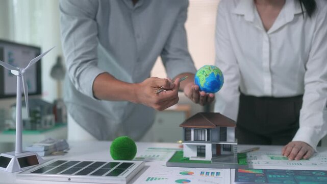 Engineers discussing clean energy for residential home models using wind turbines, solar panels and an earth globe