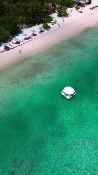 Aerial floating dome near shoreline, white dome in shallow turquoise water, lined umbrellas and sunbeds on white sand, palm fringe and resort vibe, drone hospitality shot, vertical video
