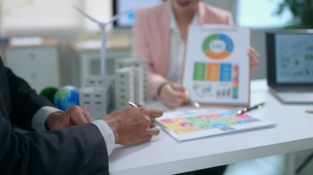 Businessman calculating costs for sustainable energy project while coworker presents ESG data during meeting
