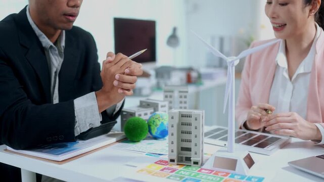 Engineers planning green energy project with wind turbine and solar panel models in a corporate meeting