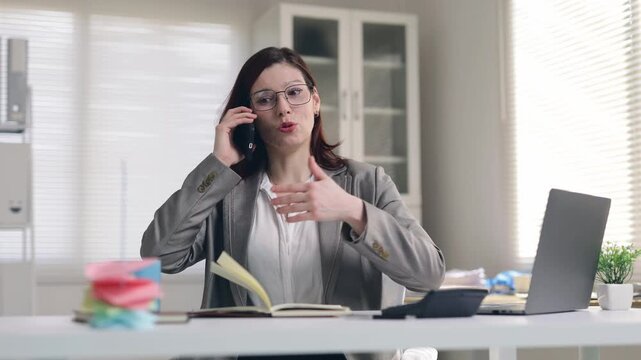 Stressed businesswoman talking angrily on the phone at her office desk with a laptop and documents