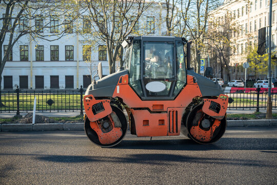Heavy machinery working on paving main city roads, workers busy finishing pave process.