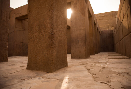 Low angle view of massive ancient temple stone columns with a dramatic light shaft piercing the ruins interior ideal for Egypt travel and archaeology