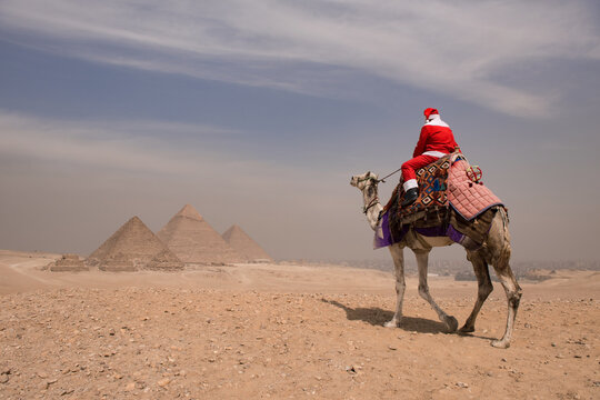 Santa claus riding a decorated camel across the arid Giza desert plateau with the ancient pyramids in the misty background