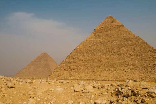 Two majestic pyramids of Giza dominating a wide rocky desert terrain under hazy blue sky offering generous copy space for Egypt travel education and