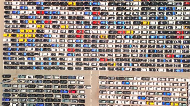 A drone pulls back revealing a massive storage terminal packed with thousands of new cars