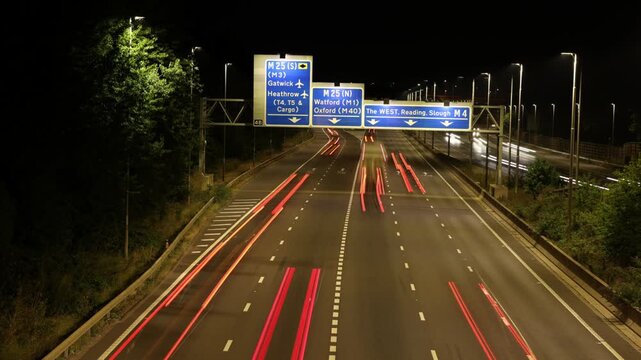 A Time-Lapse Shot of Traffic Light Trails on a British Motorway at Night, Showing Illuminated Overhead Gantry Signs Directing Traffic to Heathrow Airport, Gatwick Airport, and the M4