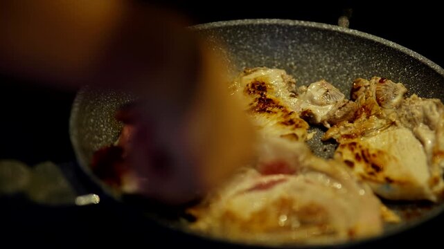 Hand Flipping Sizzling Meat Pieces In Hot Frying Pan. Cooking Pork Chops 