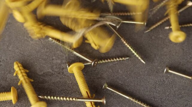 Quick-installation construction dowels with metal screws fall on a concrete surface. Quick-installation kits (dowel-nail) yellow. Close-up of fasteners for construction work