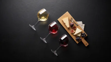 Top-down view of three wine glasses and a cheese pairing board with figs on dark slate, ideal for luxury winery tasting event advertising. © Tania Zbrodko