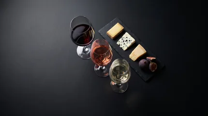 Top-down view of three wine glasses and a cheese pairing board with figs on dark slate, ideal for luxury winery tasting event advertising. © Tania Zbrodko