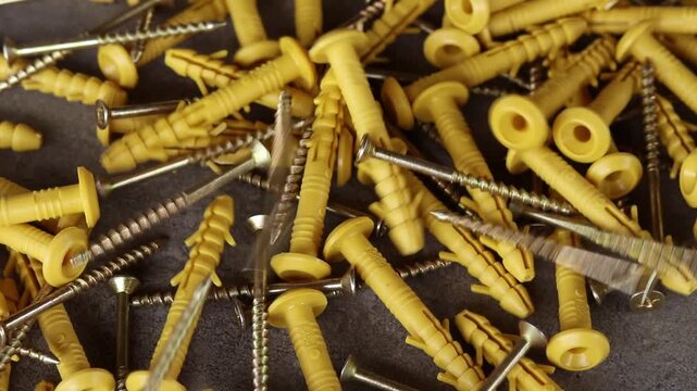 Yellow plastic dowels with metal screws fall on a gray surface. Top view of scattered construction fasteners. Dowel with a screw for quick installation. Close-up of fasteners for construction work