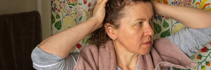 Fototapeta premium A 50-year-old woman prepares for her day in her bathroom. She is focused while removing a towel from her hair. The room is bright and colorful, reflecting a cheerful atmosphere, banner