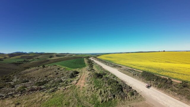 Aerial drone shot of two active cyclists ride along a gravel road between lush agricultural farmlands