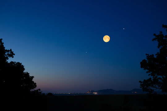 Full Moon on a twilight sky with landscape silhouettes.