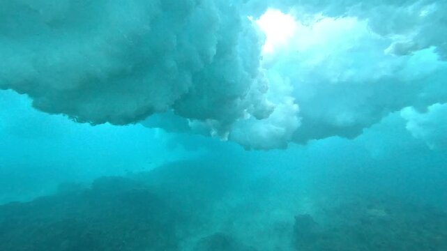 UNDERWATER: Turquoise light filters through a cloud of foam as breaking wave detonates above the tropical reef. Raw power and bubbly texture of ocean at a remote surf spot in the Mentawai Islands.