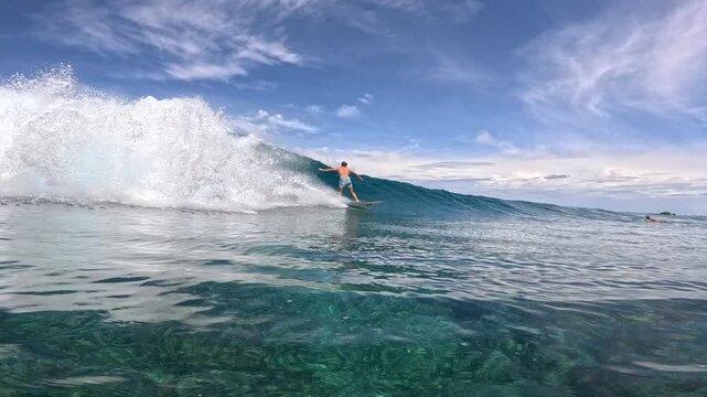 SLOW MOTION: Male surfer in shorts carving along a clean tropical wave as white spray rises behind him. Speed, balance and pristine beauty of a remote Mentawai surf spot in West Sumatra, Indonesia.