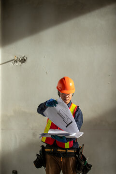 Construction engineer examining architectural plans while wearing safety equipment and a hard hat at a building site