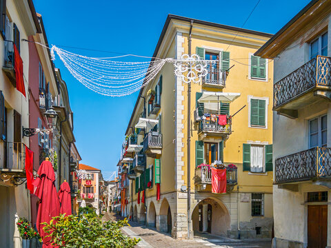 Pedestrian street Contrada Mondovi in Cuneo, Piedmont, Italy, featuring traditional yellow and red buildings, classic green window shutters, historical stone arches, and festive decorations
