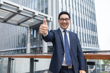 Fototapeta premium Smiling businessman giving thumbs up outside modern office building