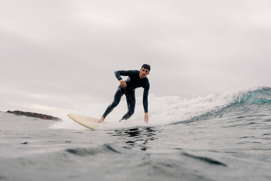 A man in a black wetsuit balances on a surfboard riding a wave.