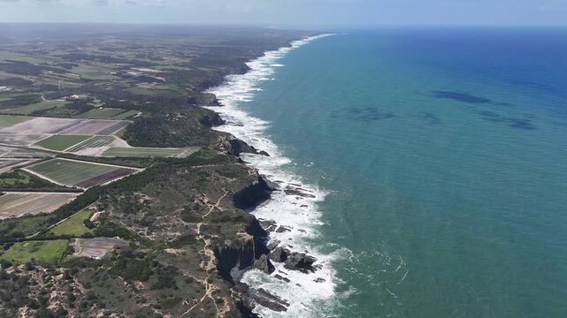 An aerial push in drone shot reveals the rugged coastline of Portugal's Fisherman's Trail near Odeceixe. Witness the wild beauty of the Rota Vicentina with crashing ocean waves against cliffs.
