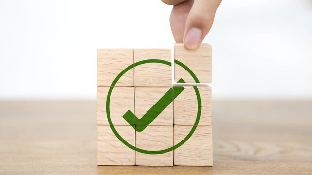 Close-up of a hand placing the final wooden block to complete a green checkmark icon graphic, representing project completion, success, task execution, quality assurance, and goal achievement.