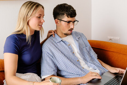 A woman leans on a man's shoulder as they look at a laptop screen.