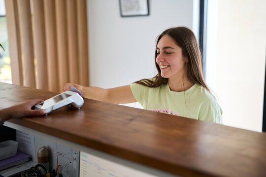 Young woman making contactless payment at reception desk