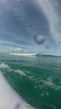 VERTICAL, FPV, SLOW MOTION: Male surfer paddling back to the lineup after a surf ride. White board, arm stroke and turquoise water frame a breaking wave ahead at remote tropical surf spot in Indonesia