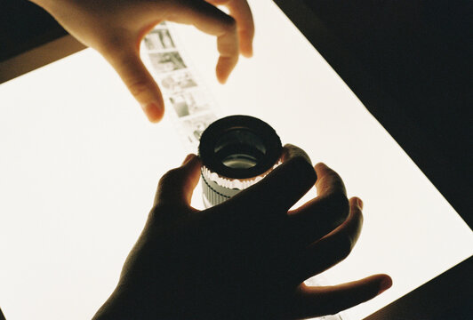 Hands holding a film loupe over contact sheet negatives