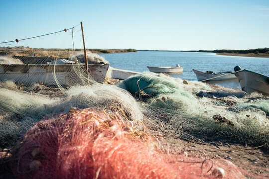 red fishing net and white boats on sandy beach under blue sky
