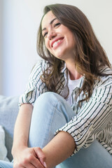 Fototapeta premium Smiling young woman sitting casually at home, relaxed and happy in a striped shirt and jeans, enjoying a peaceful moment