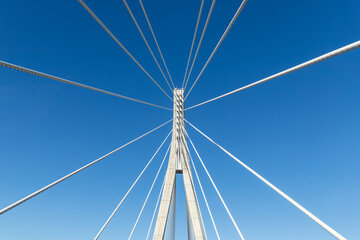 Fototapeta premium Cable bridge pylon rises into clear blue sky with steel supports forming symmetrical geometry. Minimal industrial view highlights engineering infrastructure tension modern design, and Germany travel