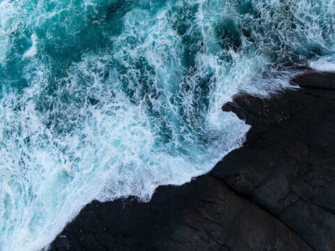 Turquoise ocean waves crashing against dark coastal rocks