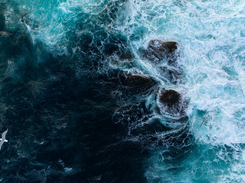 Aerial view of turbulent ocean waves over dark coastal rocks