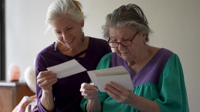 Mature daughter shares photos and stories with her elderly mother during a visit at a senior care facility. They enjoy their time together.